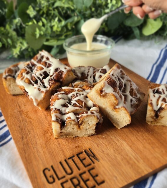 Gluten-free Cinnamon Roll Focaccia with icing drizzle on a wood board with a bowl of icing in the background