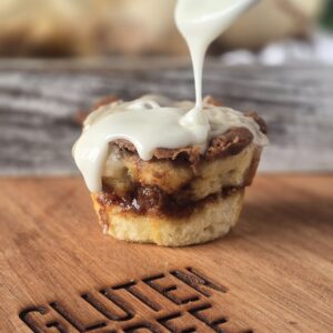 gluten free cinnamon roll muffins with icing being drizzled on top